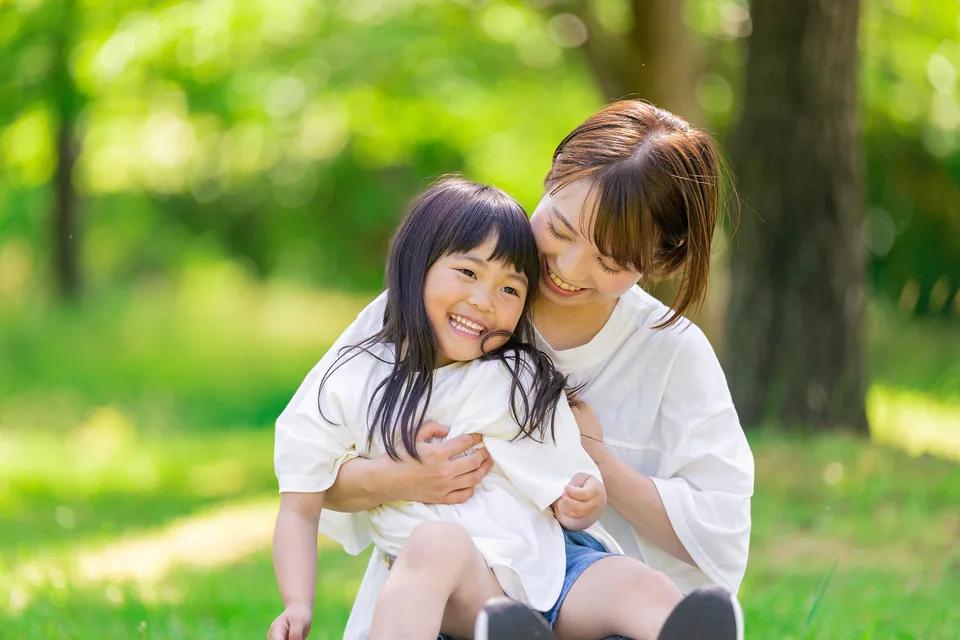 屋外で子どもを抱きしめて笑う母親