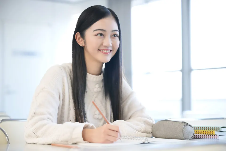 自宅の机でノートを広げ、笑顔で学習する女性